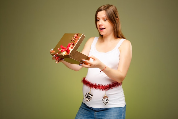 Беременная женщина с подарком с удивленным выражением лица получает подарок в канун Рождества