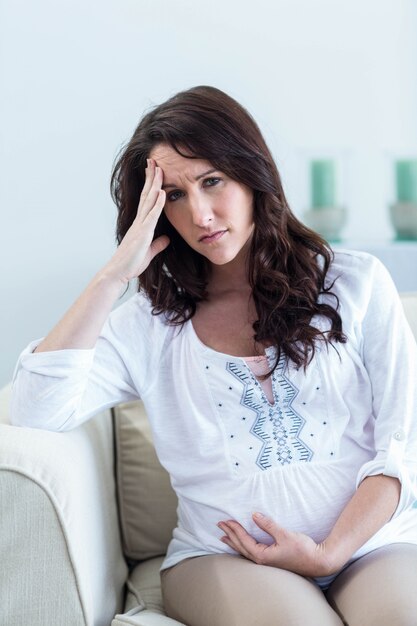 Pregnant woman with headache sitting on sofa