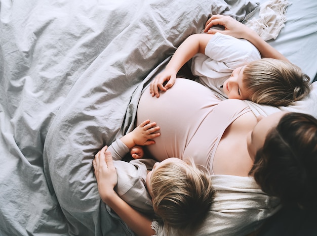 Беременная женщина с детьми, отдыхая в постели Любящая мать и малышей вместе дома
