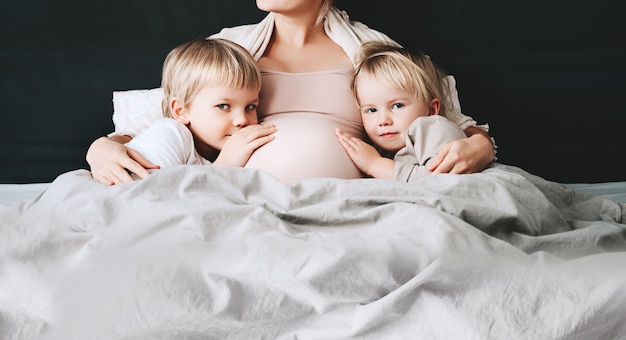 Фото Беременная женщина с детьми, отдыхая в постели любящая мать и малышей вместе дома