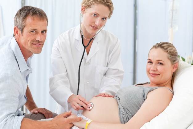 Pregnant woman with her husband and the nurse looking at the camera