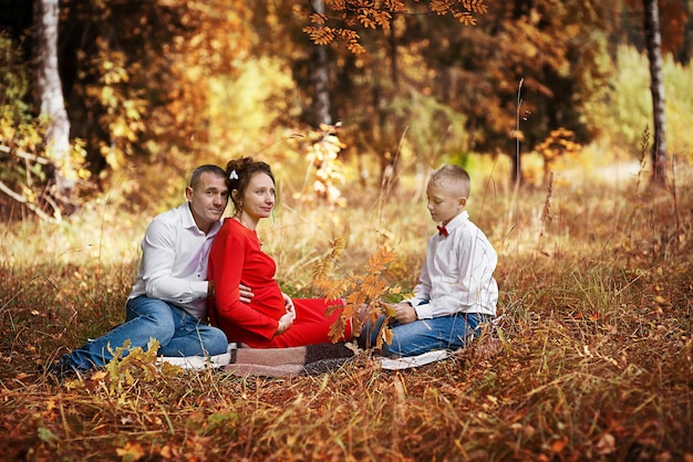 A pregnant woman with her husband and son in an autumn park