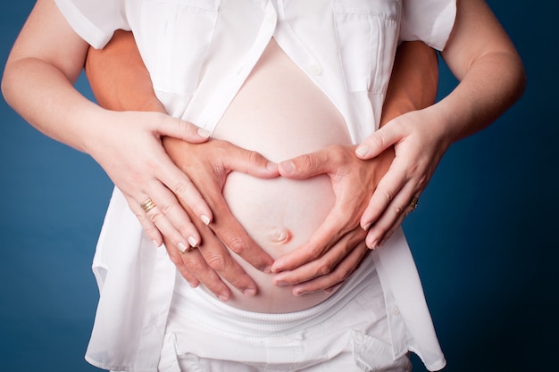 Pregnant woman with her husband with a heart shaped with hands