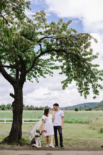 Pregnant woman with husband and husky dog near tree in nature