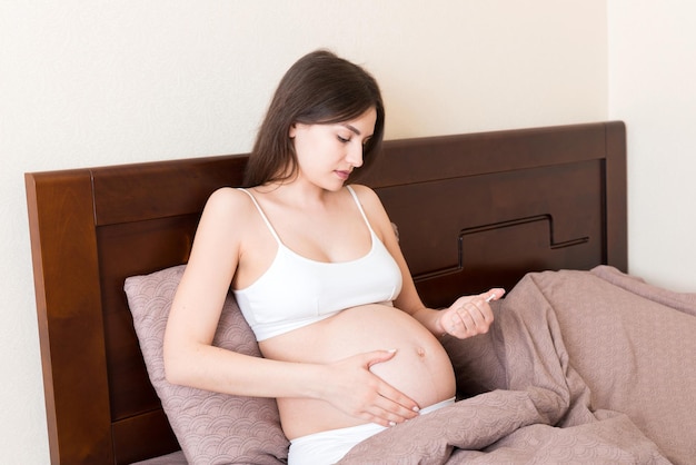 Pregnant woman with insulin syringe in home on bed Pregnant diabetes concept