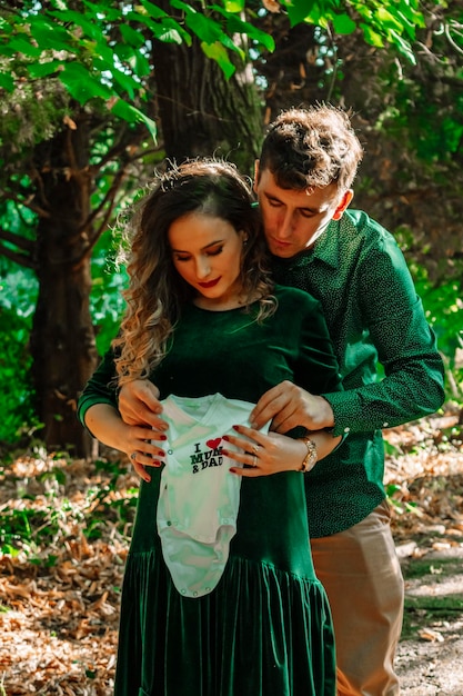 Foto donna incinta con un uomo che tiene i vestiti del bambino nella foresta