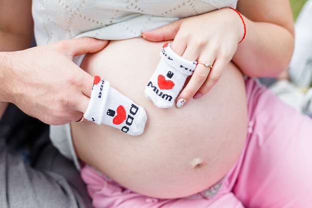 Pregnant woman with a man, put hands with socks close-up on belly