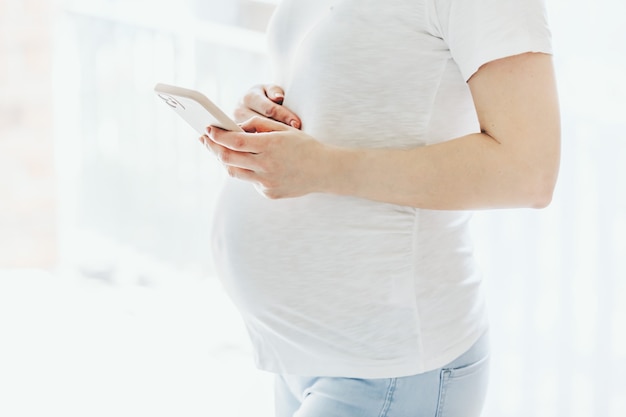 Беременная женщина с мобильным телефоном, оставаясь дома