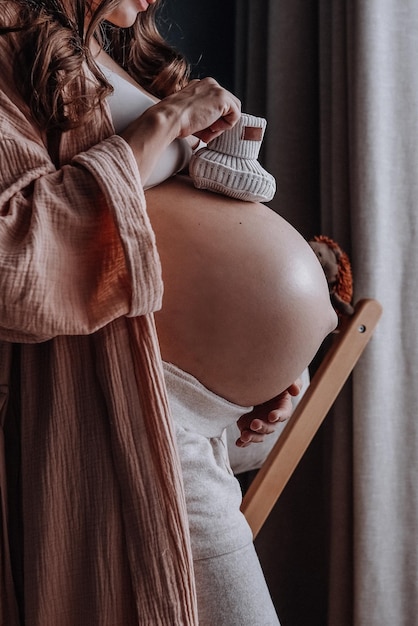 Pregnant woman with mug of hot herbal tea staying in front of window expecting new baby