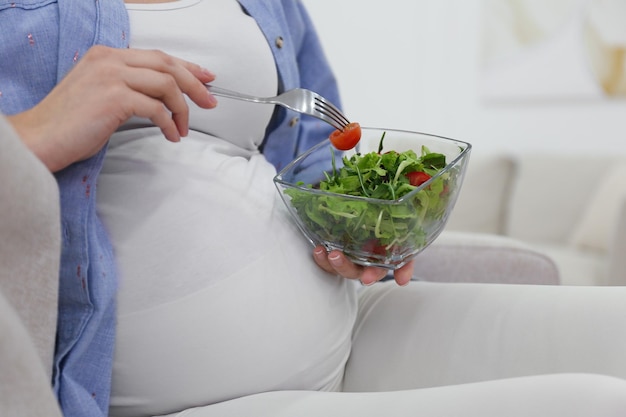 Pregnant woman with salad on sofa at home closeup Healthy diet