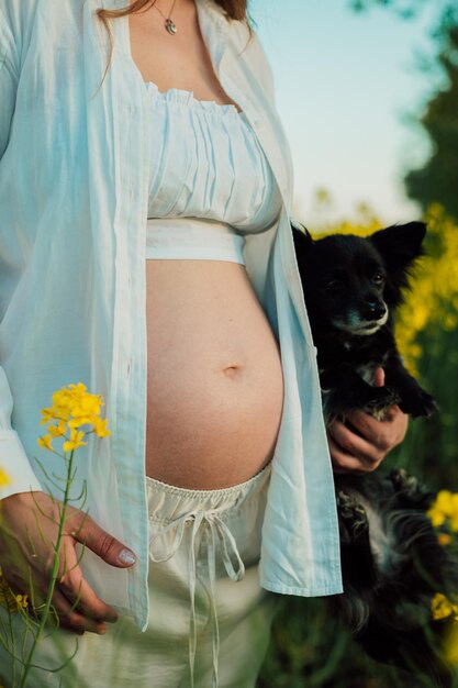 Photo a pregnant woman with a small black dog in nature rapeseed field