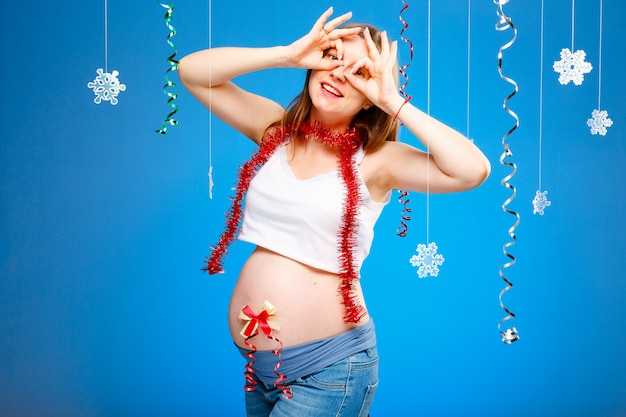 Foto donna incinta con fiocchi di neve su sfondo blu e ghirlanda rossa aspettando un bambino a natale