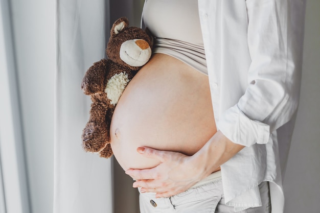 赤ちゃんを聞いているおもちゃのテディベアを持つ妊婦。ライフスタイル。マタニティの概念。