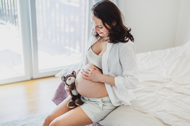 赤ちゃんを聞いているおもちゃのテディベアを持つ妊婦