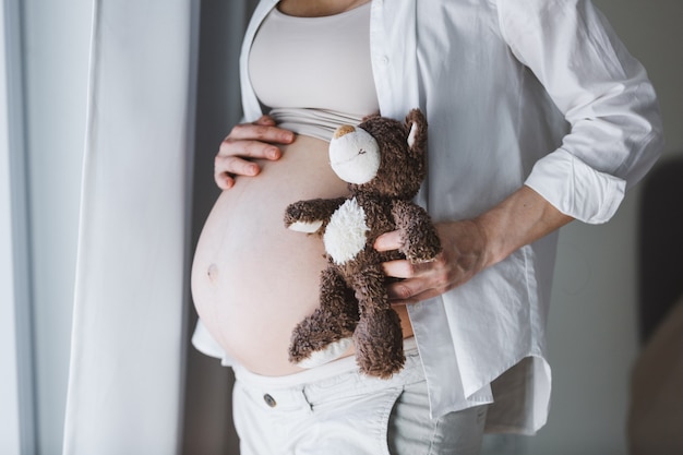 赤ちゃんを聞いているおもちゃのテディベアを持つ妊婦