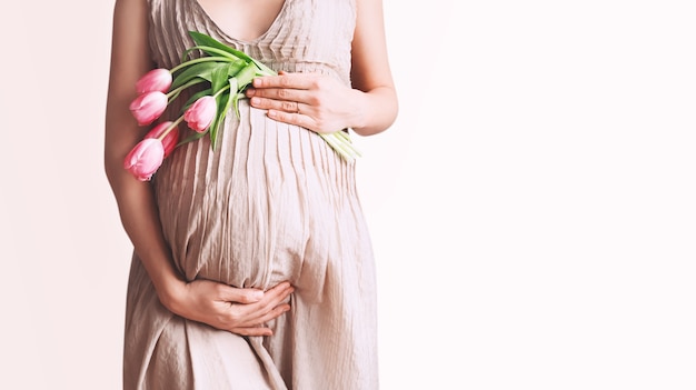 チューリップと妊娠中の女性は、腹妊娠母の日の休日の概念に手を握る