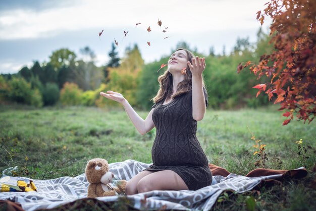 おなかの妊娠中の女性は毛布の上に座って、黄色の葉をスローします