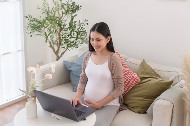 Pregnant woman working on laptop and smart phone in the living room at home