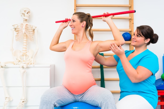 Pregnant woman working out in physiotherapy with gymnastic stick