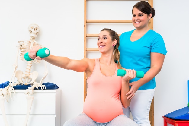 Беременная женщина работает с гантелями в физиотерапии