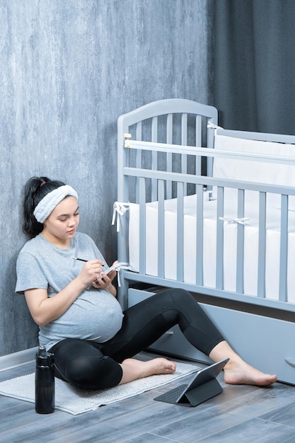 A pregnant woman writes in a notebook and watches videos on a tablet