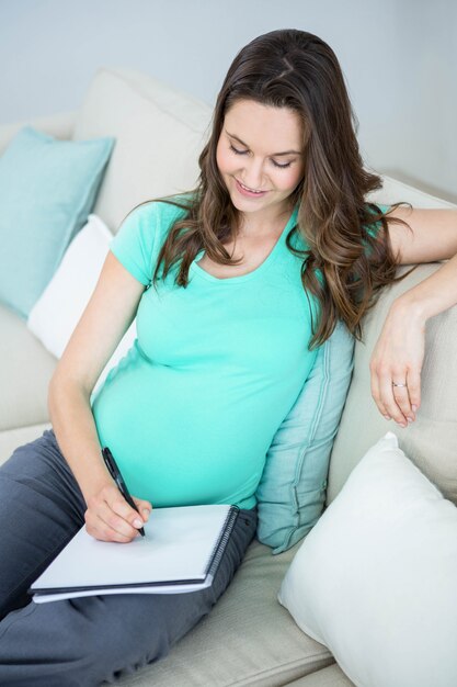 Pregnant woman writing on document on couch