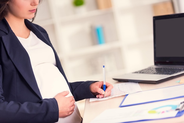 写真 妊娠中の女性がオフィスの机に書いています