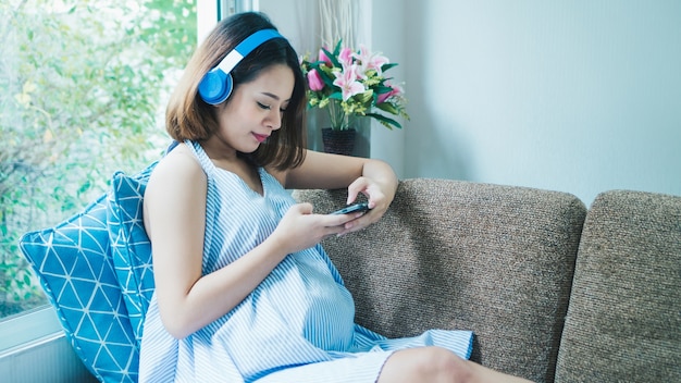 Pregnant women are listening to music on the couch and playing mobile phones.