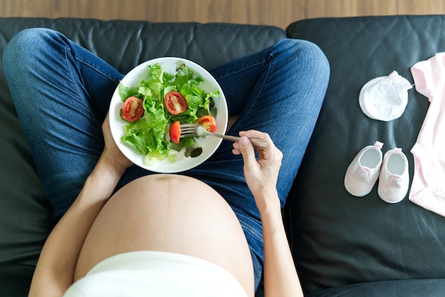 Pregnant women is holding salad bowl in her hand.