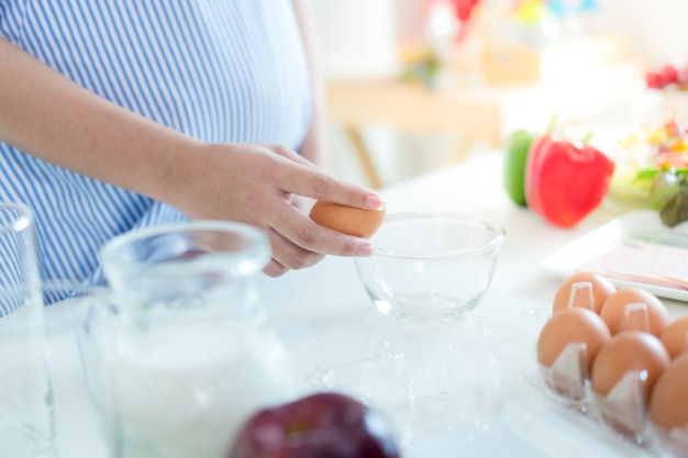 Photo pregnant women put on a blue dress. she is egg whip in the kitchen. there is apple, chili.