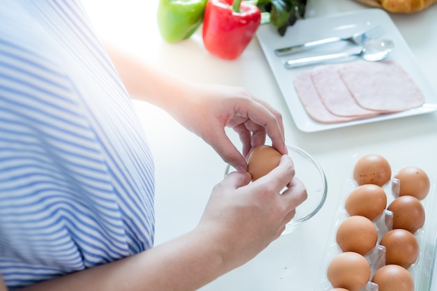 Photo pregnant women put on a blue dress. she is smashing eggs make breakfast in the kitchen.