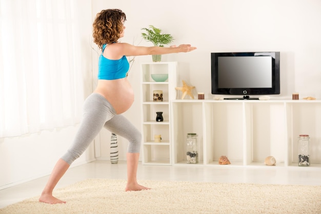 Pregnant women in sportswear, doing exercises in the living room.