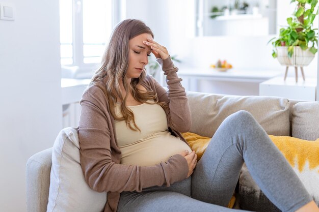 Pregnant young adult woman resting on sofa at home feeling unwell