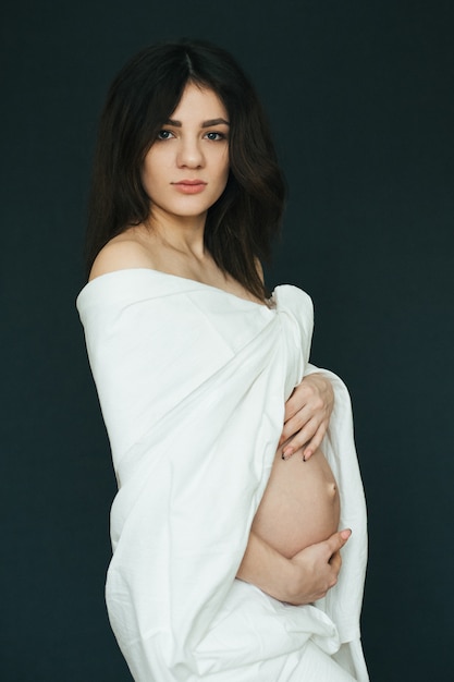 Беременная молодая красивая брюнетка девушка в белой ткани