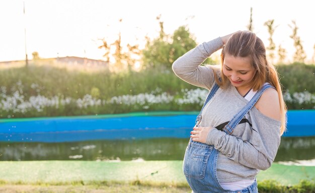 Giovane donna incinta che abbraccia il suo stomaco all'aperto