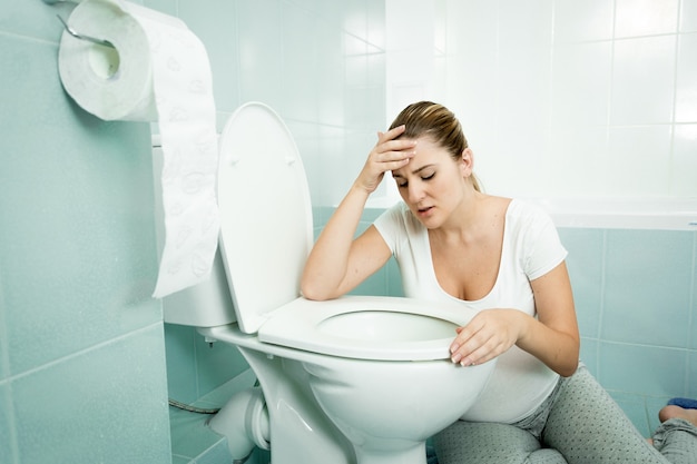 Фото Беременная молодая женщина, опираясь на туалет и чувствуя себя больным