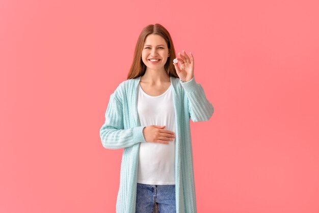 Pregnant young woman with pill on color surface