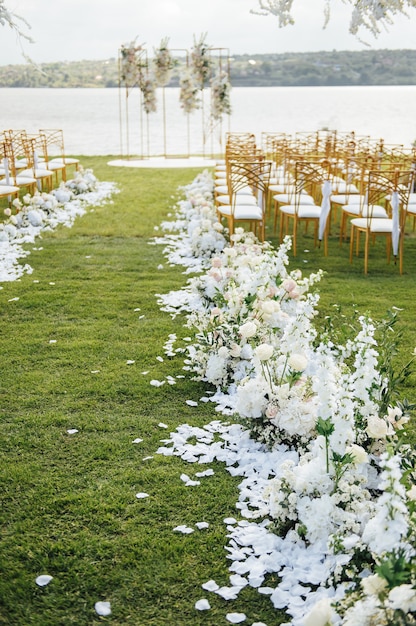 Arco premium per cerimonia nuziale per sposi novelli sulla riva del fiume con alberi di glicine. sedie e ombrelloni vuoti