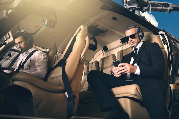Foto l'attività premium richiede un trasporto premium inquadratura di un uomo d'affari maturo che utilizza un telefono cellulare mentre viaggia in elicottero