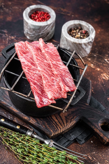 Premium raw sliced wagyu beef A5 steaks on a grill for yakiniku. Japanese foods. Dark background. Top view.