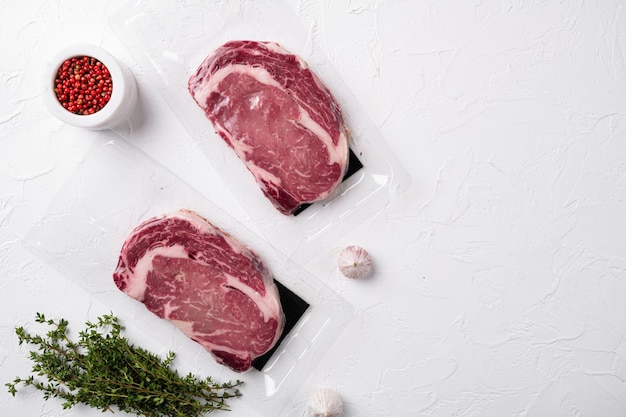 Premium rib eye steak in a vacuum pack set, on white stone table background, top view flat lay, with copy space for text