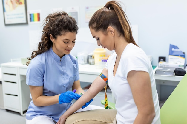 Preparation for blood test with pretty young woman by female doctor medical uniform on the table in white bright room Nurse pierces the patient's arm vein with needle blank tube