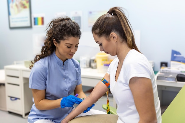Photo preparation for blood test with pretty young woman by female doctor medical uniform on the table in white bright room nurse pierces the patient's arm vein with needle blank tube