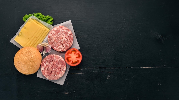 Preparation of burger Meat fresh vegetables tomatoes onions On a black wooden background Top view Free copy space