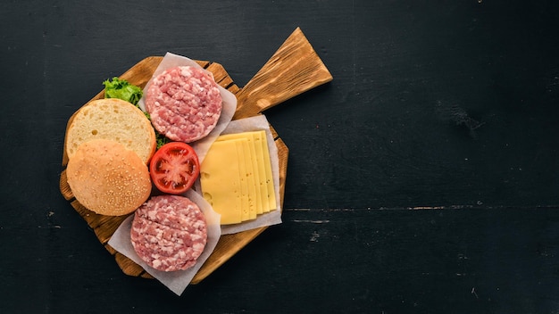 Preparation of burger Meat fresh vegetables tomatoes onions On a black wooden background Top view Free copy space