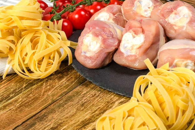 Preparation chicken. Raw chicken drumsticks, homemade dry macaroni, branch of red tomato l