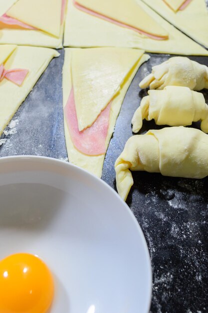 Preparation of croissants with ham and cheese painted with egg yolk on wooden board ready to bake