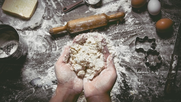 Preparation of dough. dough women's hands and tools. sieve, rolling pin, knife, whisk on wooden table. Top view