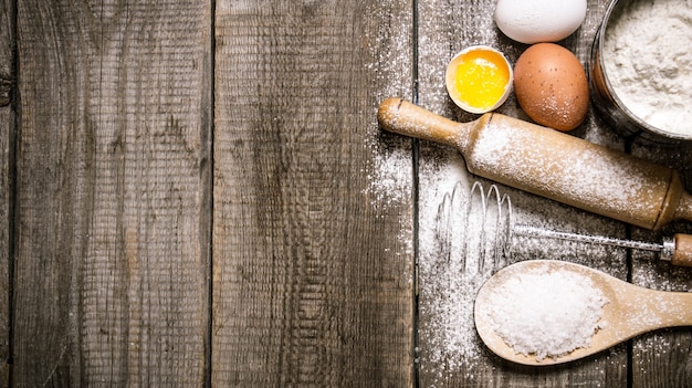 Preparation of the dough. Ingredients for the dough - Eggs and flour with a rolling pin. On wooden background. Free space for text . Top view