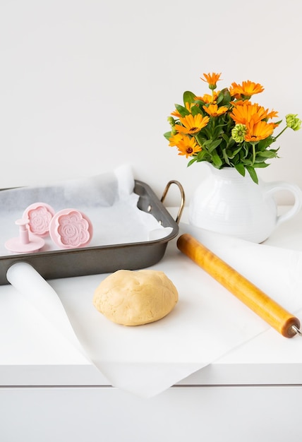 Preparation of the dough for making cookies with molds in the form of flowers a rolling pin a bouquet of orange flowers and a baking tray Concept of family and cooking